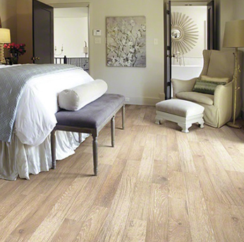 A bright bedroom with light wood flooring, a grey bench, and an armchair.