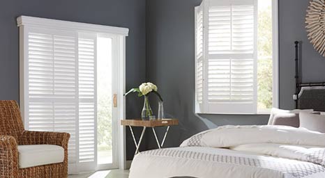 Bedroom with white louvered plantation shutters on windows and sliding doors