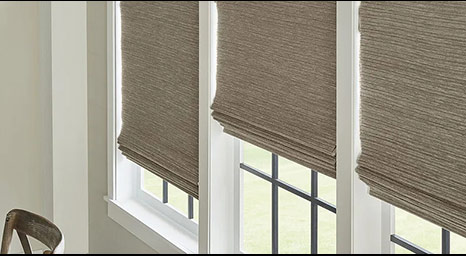 Woven brown natural fiber shades hanging in white window frames.